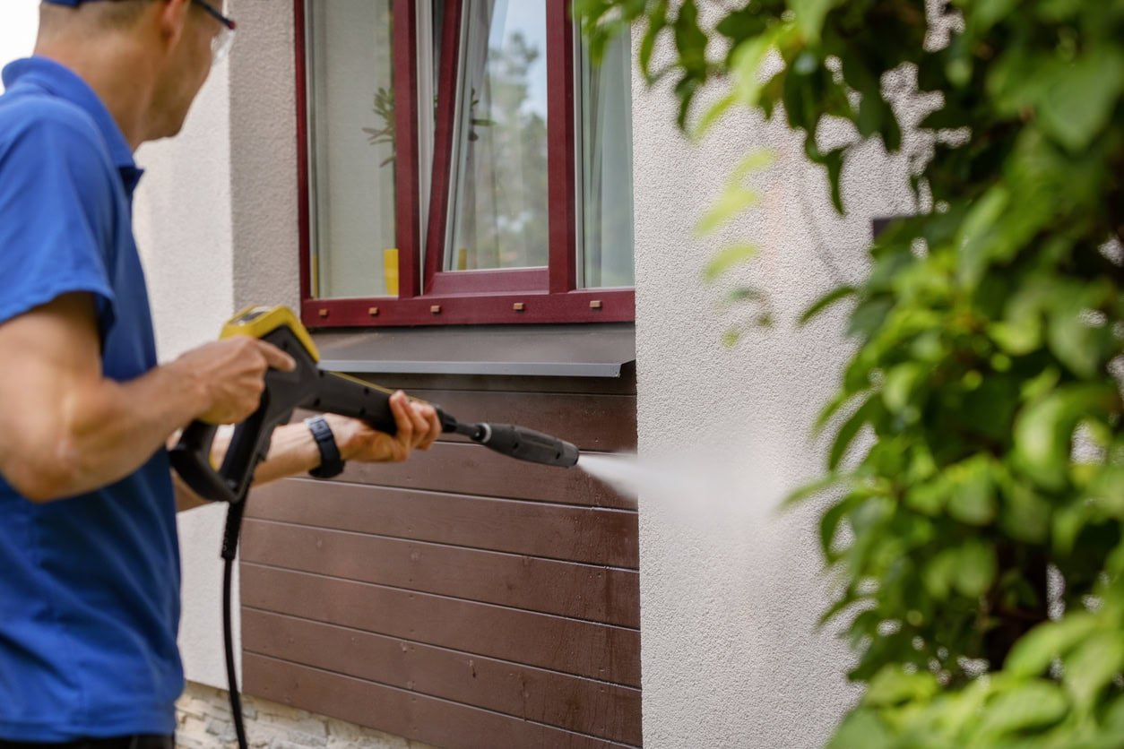 Hombre utilizando un hidrojet para limpiar una pared exterior, representando los servicios profesionales de limpieza de residencias en Madrid.